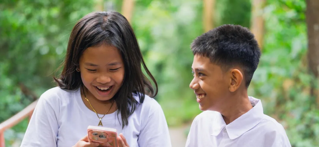 Young people work together on a small electronic device outdoors in a rural setting.